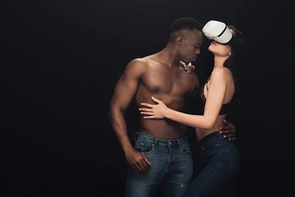 African american man hugging sexy woman in virtual reality headset isolated on black with copy space — Stock Photo