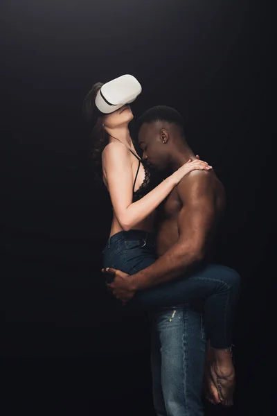 Shirtless african american man hugging sexy woman in virtual reality headset isolated on black — Stock Photo