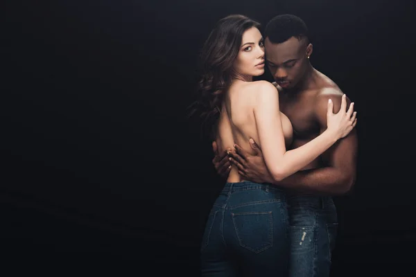 Beautiful seductive half-naked interracial couple embracing isolated on black with copy space — Stock Photo