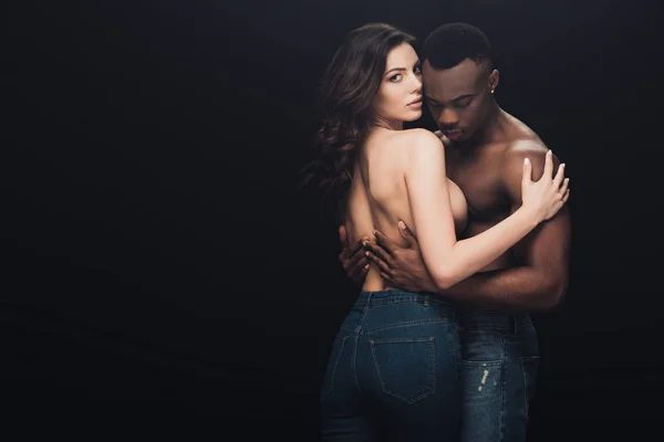 Hermosa seductora pareja interracial semidesnuda abrazando aislado en negro con espacio de copia - foto de stock