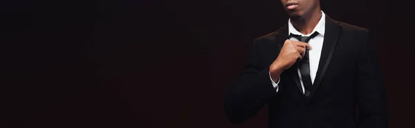 Cropped view of fashionable african american man in suit adjusting tie isolated on black with copy space — Stock Photo