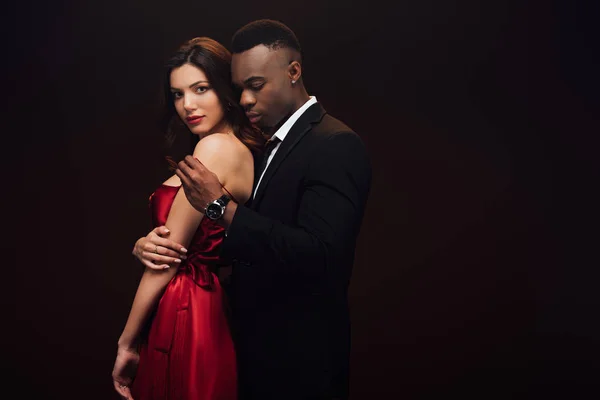 Africano americano hombre desvestirse hermosa mujer en rojo vestido aislado en negro con copia espacio - foto de stock