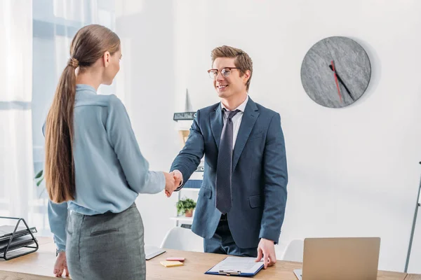 Woman shaking hands with cheerful recruiter in glasses standing near table — Stock Photo