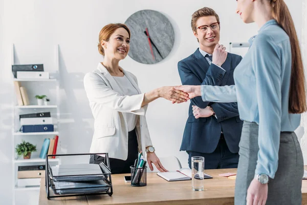 Vista recortada de la mujer estrechando la mano con reclutador alegre cerca de compañero de trabajo guapo en gafas - foto de stock