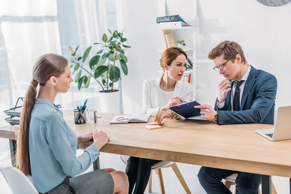 Handsome recruiter in glasses holding clipboard near woman while speaking near attractive employee — Stock Photo