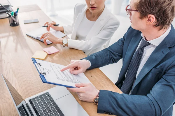 Cropped view of recruiter in glasses pointing with finger at clipboard near coworker — Stock Photo