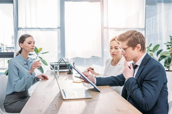 Pensive hr in glasses looking at clipboard near women during job interview — Stock Photo