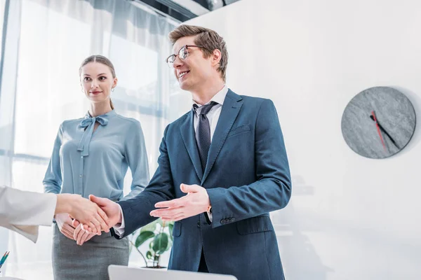 Low angle view of cheerful recruiter shaking hands with woman near attractive colleague in office — Stock Photo
