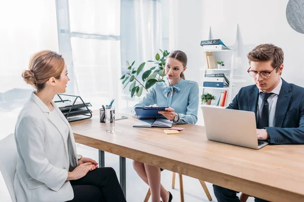 Woman talking with recruiter holding clipboard while coworker using laptop on job interview — Stock Photo