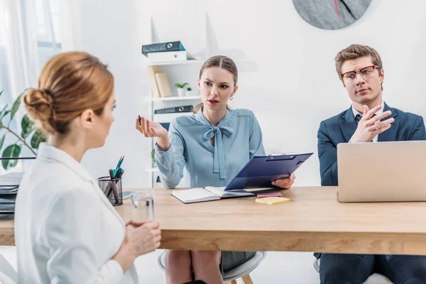 Attractive recruiter talking with woman and holding clipboard near coworker in glasses — Stock Photo