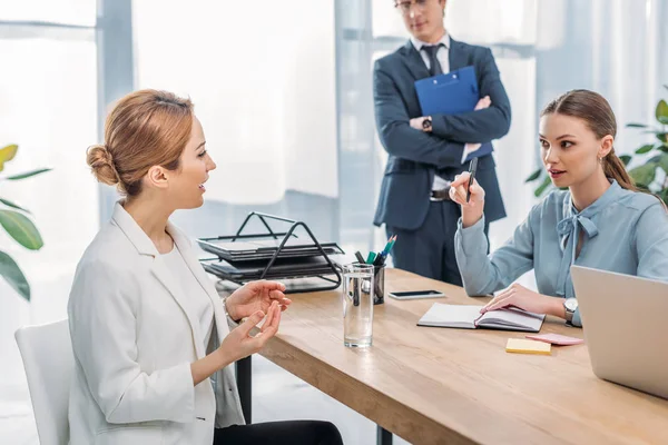 Atractiva mujer hablando con reclutador cerca de compañero de trabajo durante entrevista de trabajo - foto de stock
