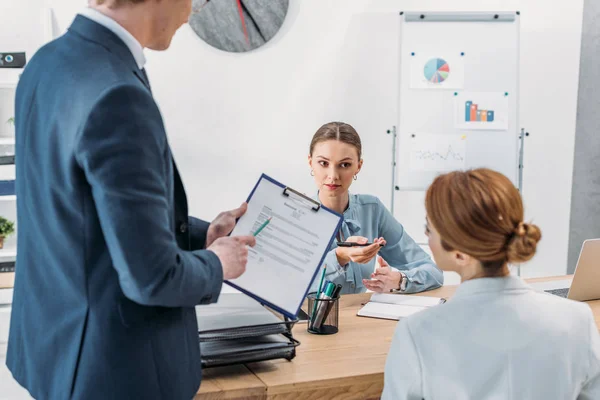 Selective focus of attractive recruiter looking at woman near coworker holding clipboard with resume cv lettering — Stock Photo