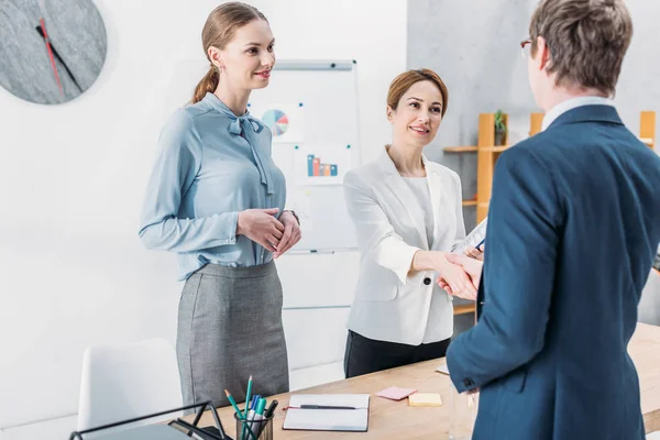 Vista posteriore di uomo che stringe la mano con il reclutatore felice vicino al collega in piedi con le mani serrate in ufficio — Foto stock