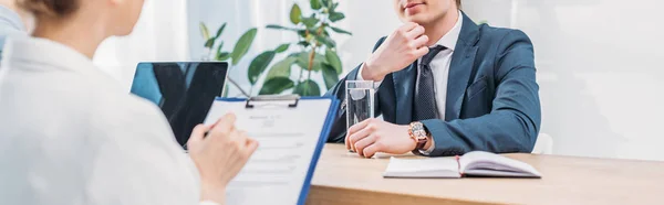 Panoramic shot of pensive employee sitting near recruiter with clipboard — Stock Photo