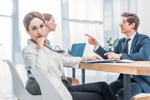 Attractive recruiter looking at camera while man in glasses pointing with finger at woman during job interview — Stock Photo