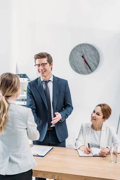 Reclutador alegre en gafas estrechando la mano con la mujer en la entrevista de trabajo - foto de stock