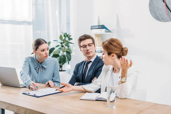 Attractive recruiter gesturing near coworker in glasses sitting with crossed arms — Stock Photo