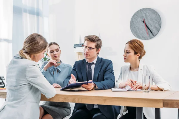 Guapo reclutador gesto mientras sostiene portapapeles y mirando a la mujer en la entrevista de trabajo - foto de stock