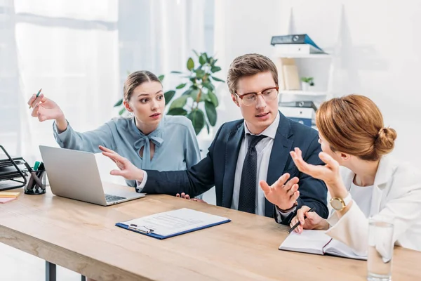 Handsome man in glasses gesturing while talking with attractive coworkers — Stock Photo