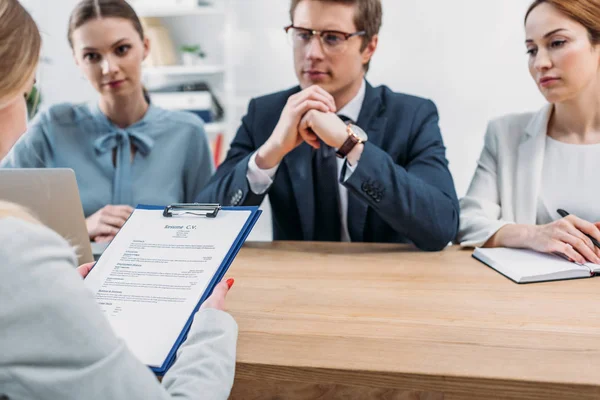 Selective focus of woman holding clipboard with resume cv lettering near recruiters — Stock Photo