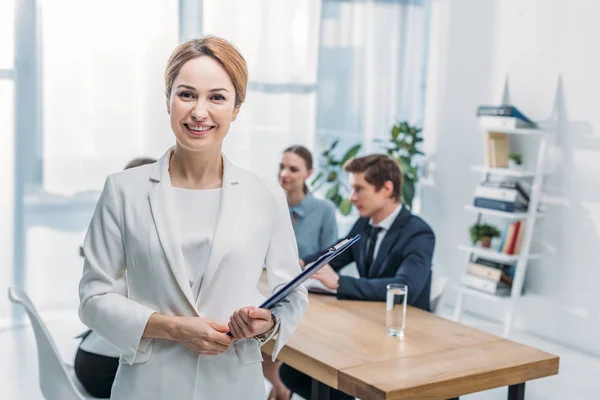 Selektiver Fokus des gut gelaunten Recruiters, der mit Klemmbrett in der Nähe von Mitarbeitern steht — Stockfoto