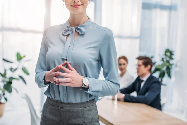 Cropped view of cheerful woman standing with clenched hands near coworkers in office — Stock Photo