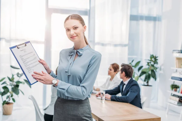 Selective focus of cheerful recruiter holding clipboard with resume cv lettering near coworkers — Stock Photo