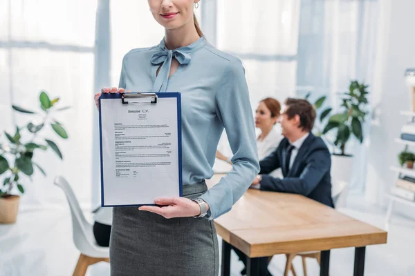 Vista cortada de recrutador alegre segurando prancheta com currículo cv lettering perto de colegas de trabalho — Fotografia de Stock