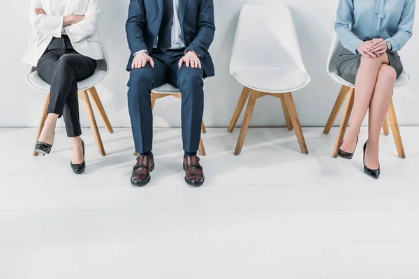 Обрізаний вид на жінок, що сидять з схрещеними ногами і схрещеними руками біля людини — стокове фото