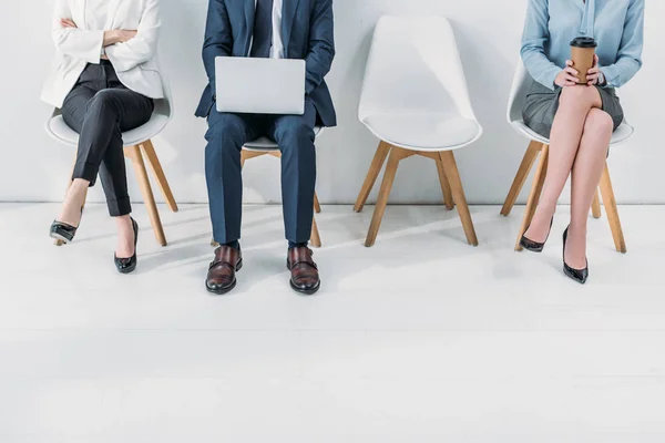 Ausgeschnittene Ansicht von Frauen, die mit überkreuzten Beinen und verschränkten Armen neben einem Mann sitzen, der Laptop benutzt — Stockfoto