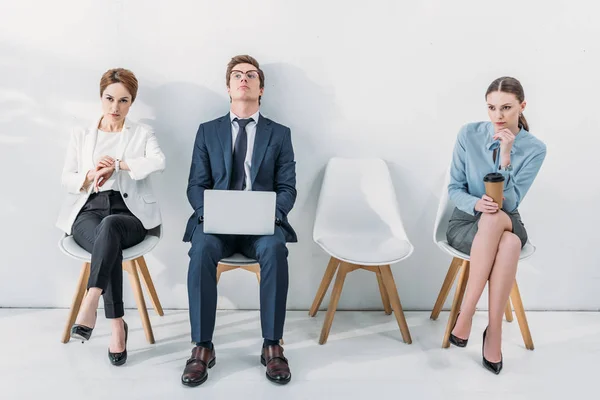 Attractive employee touching watch while sitting near man and woman — Stock Photo