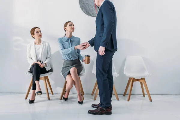 Cropped view of recruiter shaking hands with employee sitting on chair with paper cup — Stock Photo