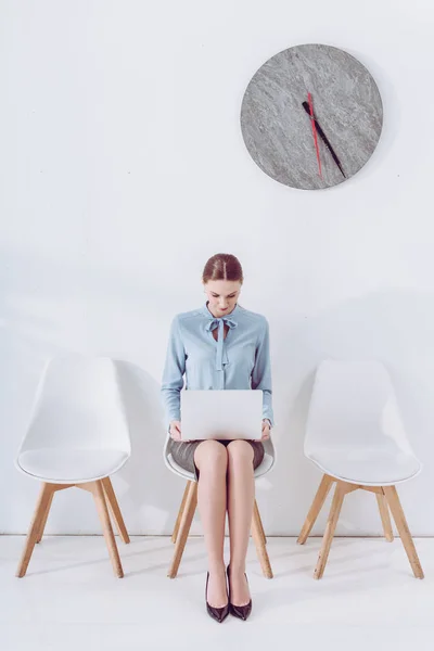 Attractive employee sitting on chair and using laptop — Stock Photo