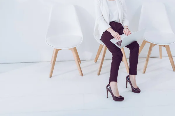 Обрезанный вид женщины, сидящей на стуле и с помощью ноутбука — стоковое фото