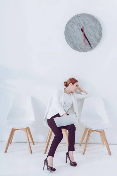 Empleado cansado sentado en la silla con el ordenador portátil y esperando entrevista de trabajo - foto de stock