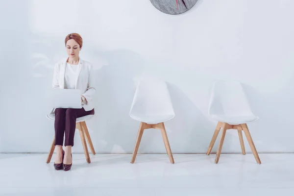 Belle employée utilisant un ordinateur portable et assise sur une chaise — Photo de stock