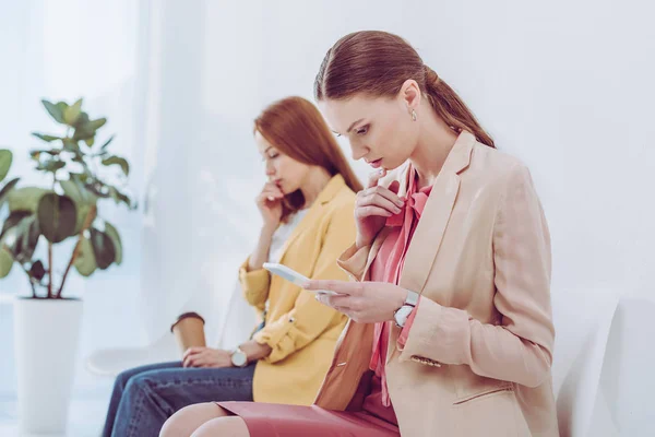 Selektive Fokussierung attraktiver Frauen mit Smartphone in der Nähe von Mitarbeitern mit Pappbecher — Stockfoto