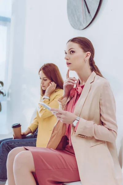 Foco seletivo da mulher pensativa usando smartphone perto de empregado com copo de papel — Fotografia de Stock