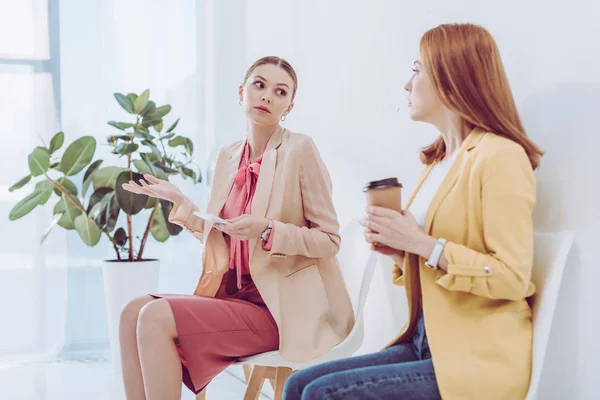 Enfoque selectivo de mujer atractiva sosteniendo teléfono inteligente y gesto cerca de empleado con taza de papel - foto de stock