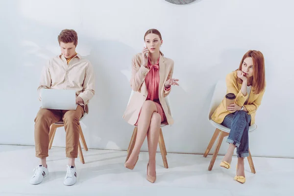 Attraktive Mitarbeiterin sitzt mit Pappbecher in der Nähe von Mann und Frau und benutzt Gadgets — Stockfoto