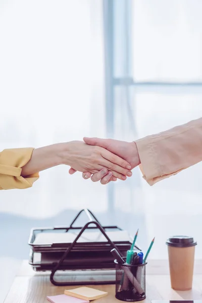 Vista recortada de reclutador y empleada mujer estrechando la mano en la oficina - foto de stock