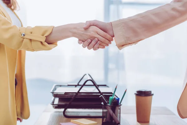 Visão cortada de empregado e recrutador apertando as mãos no escritório perto de copo de papel — Fotografia de Stock