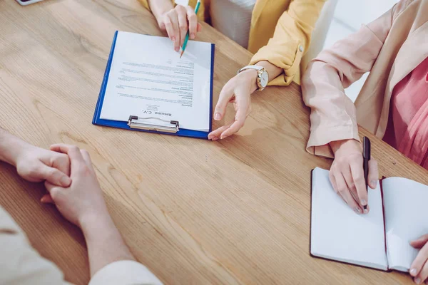 Cropped view of recruiter holding pencil and clipboard near colleague and woman on job interview — Stock Photo