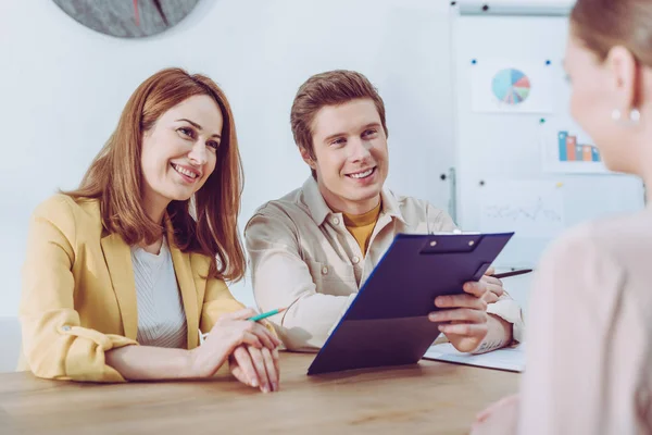 Bel reclutatore tenendo appunti vicino collega allegro durante il colloquio di lavoro — Foto stock