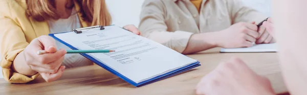 Ausgeschnittene Ansicht einer Frau, die mit Bleistift auf Klemmbrett zeigt, in der Nähe von Mitarbeiterin und Mitarbeiter — Stockfoto