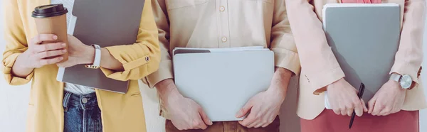 Panoramic shot of employee holding paper cup near man and woman with folders in hands — Stock Photo