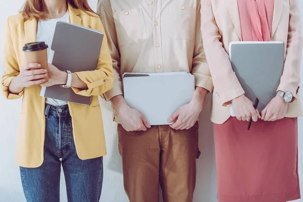 Cropped view of employee holding paper cup near man and woman with folders in hands — Stock Photo