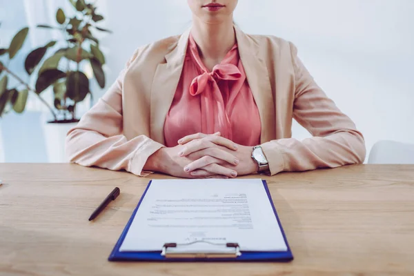 Vue recadrée du recruteur assis avec les mains serrées près du presse-papiers dans le bureau — Photo de stock