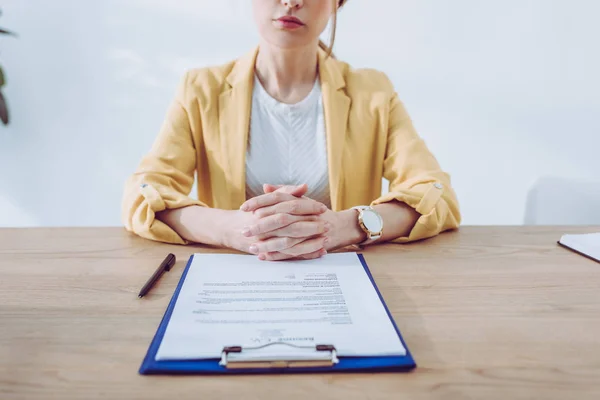 Cropped view of woman sitting with clenched hands near clipboard — Stock Photo