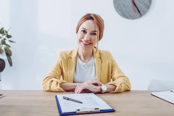 Happy recruiter in yellow jacket sitting near clipboard and pen — Stock Photo